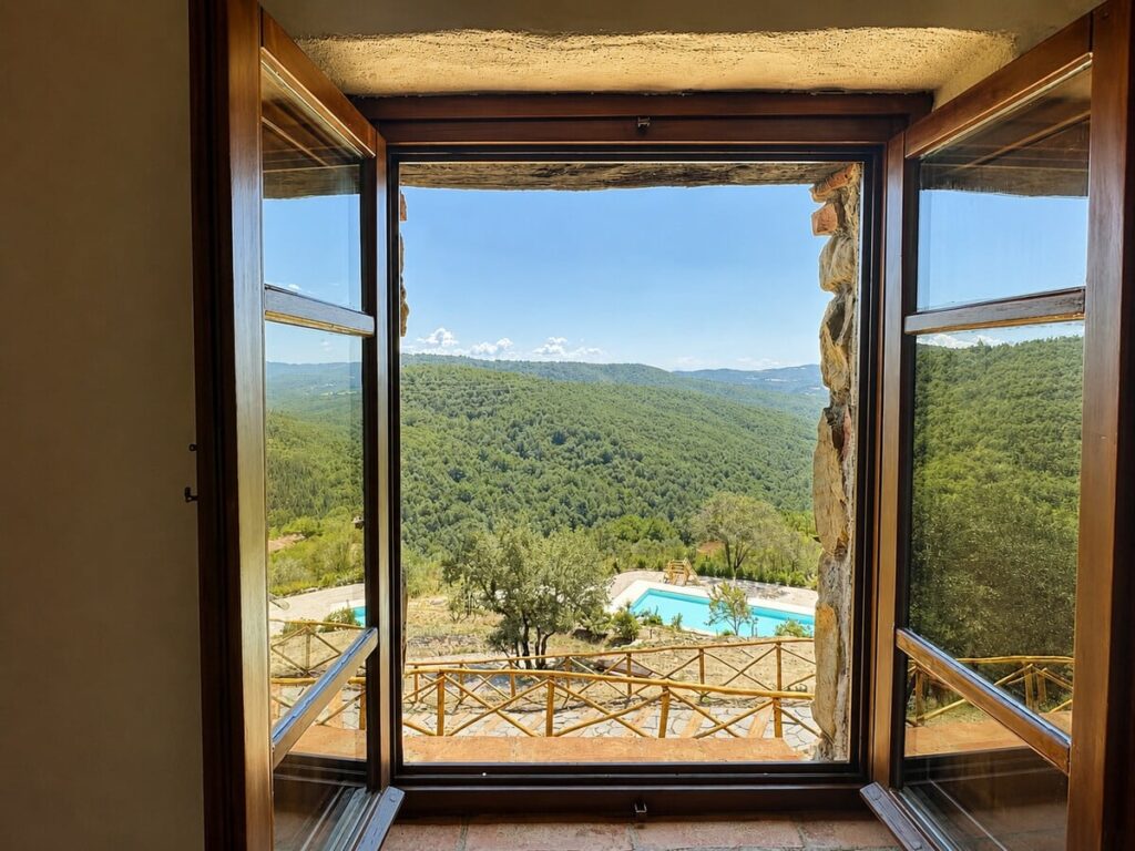 Open window with a panoramic view of the pool and hills in the Il belvedere apartment, Borgo Braila, Umbria
