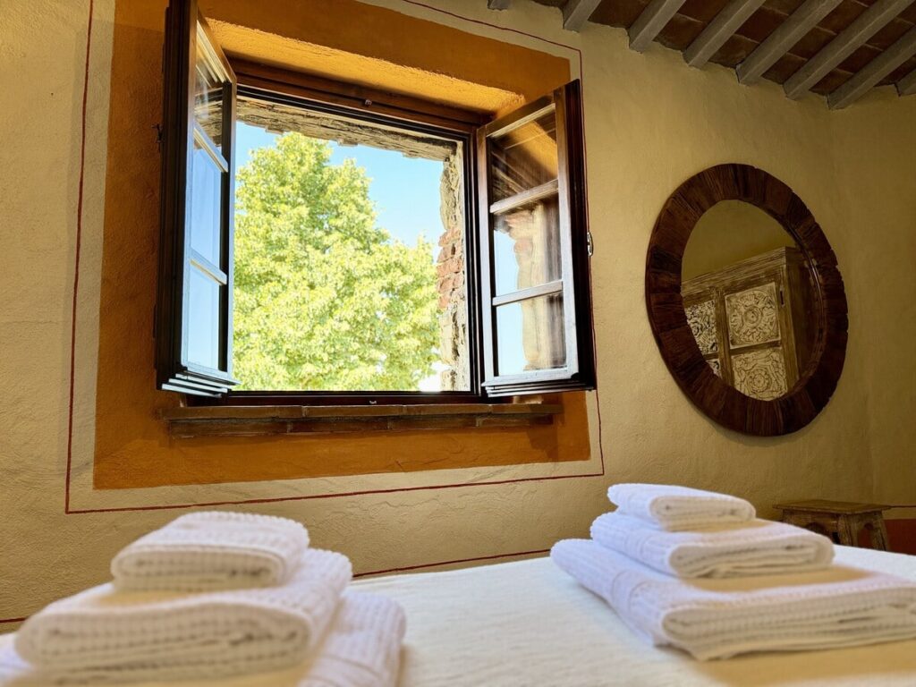 Bedroom with a window and round mirror in the La carta apartment, Borgo Braila, Umbria