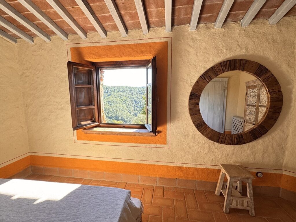 Bedroom with a round mirror and window in the La carta apartment, Borgo Braila, Umbria
