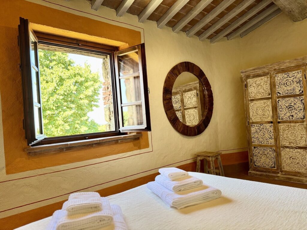 Bedroom with a window and round mirror in the La carta apartment, Borgo Braila, Umbria