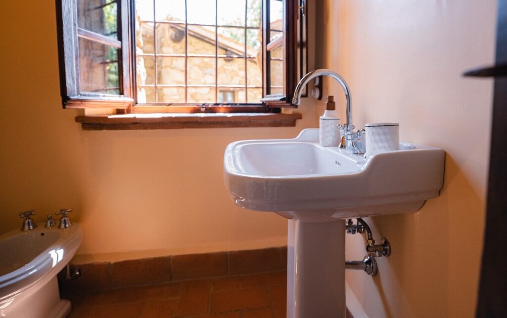 Bathroom with a pedestal sink and window in the Il cardinale apartment, Borgo Braila, Umbria